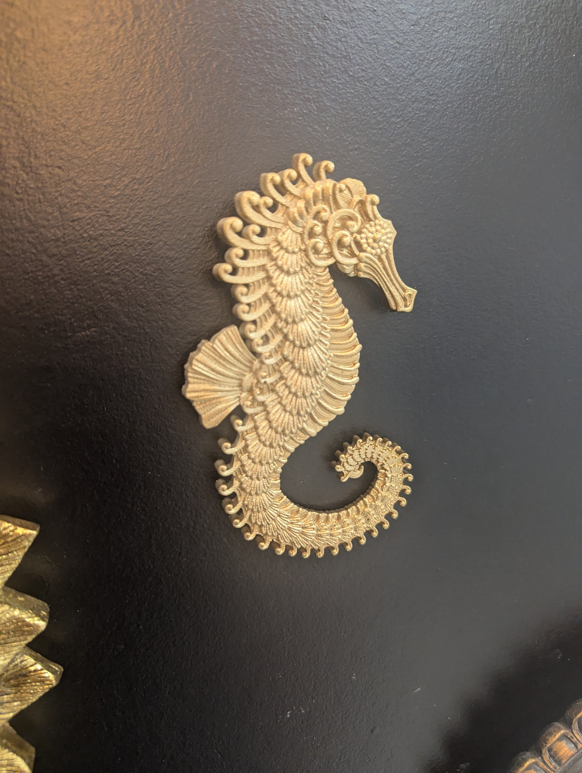 Hippocampe baroque doré accroché sur un mur noir