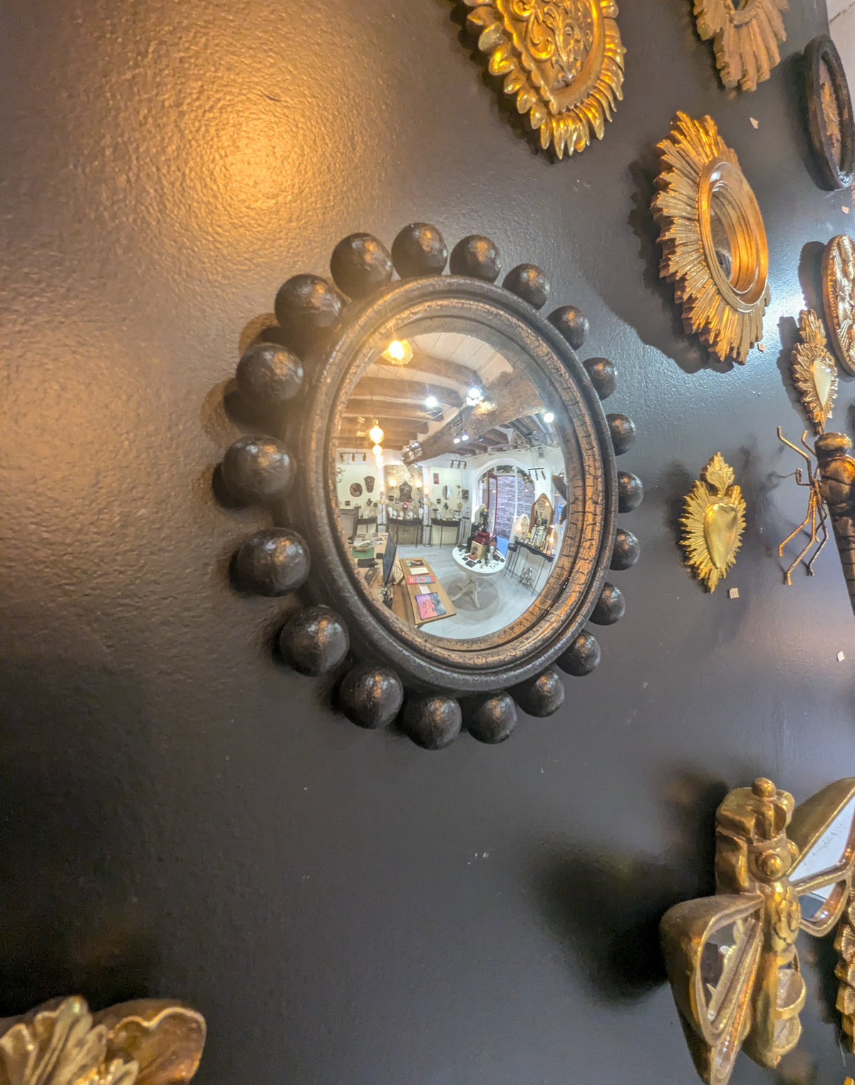 Miroir convexe noir à boules sur mur sombre avec miroirs et ornements dorés