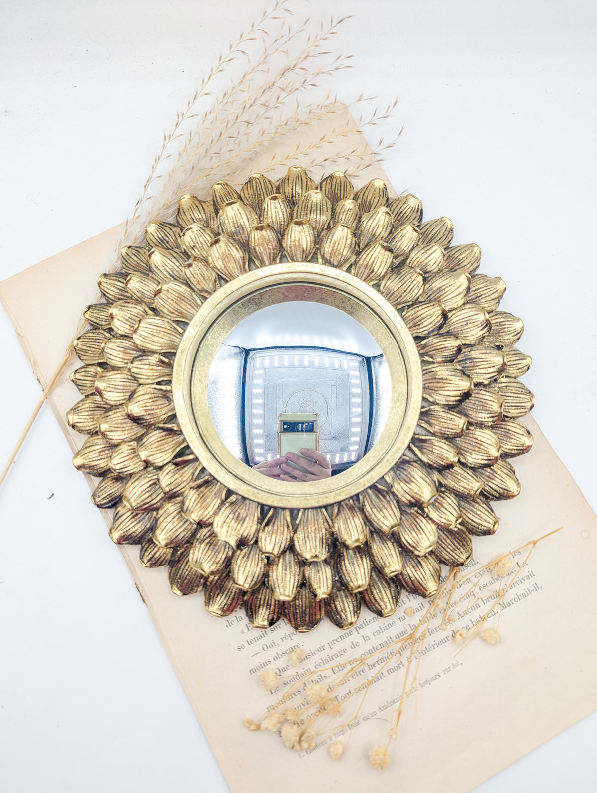 Miroir de sorcière doré à pétales de fleur posé sur un livre ancien
