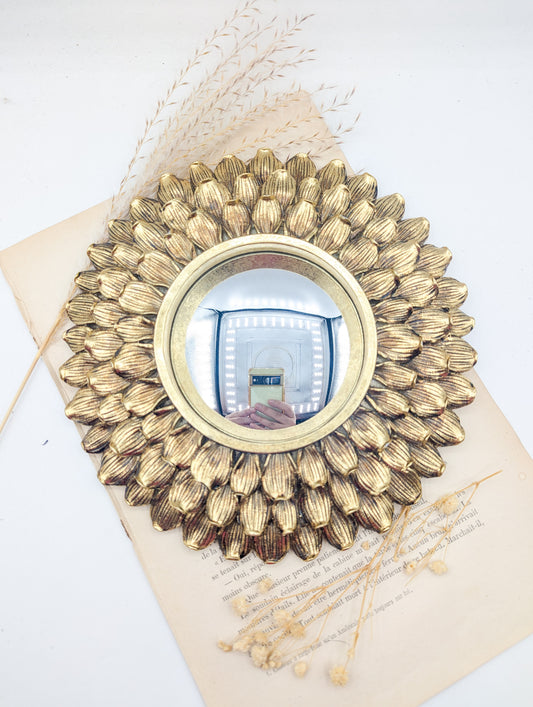Miroir de sorcière doré à pétales de fleur posé sur un livre ancien