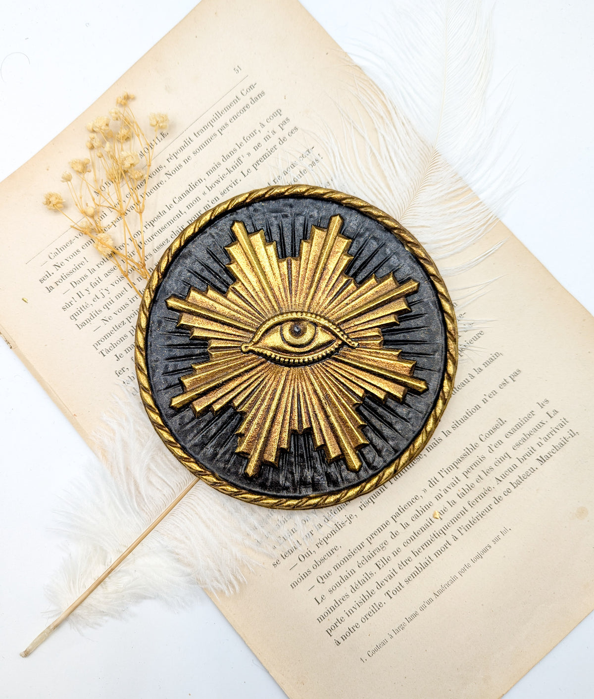 Médaillon soleil sacré doré avec œil illuminati sur fond noir, posé sur un livre ancien