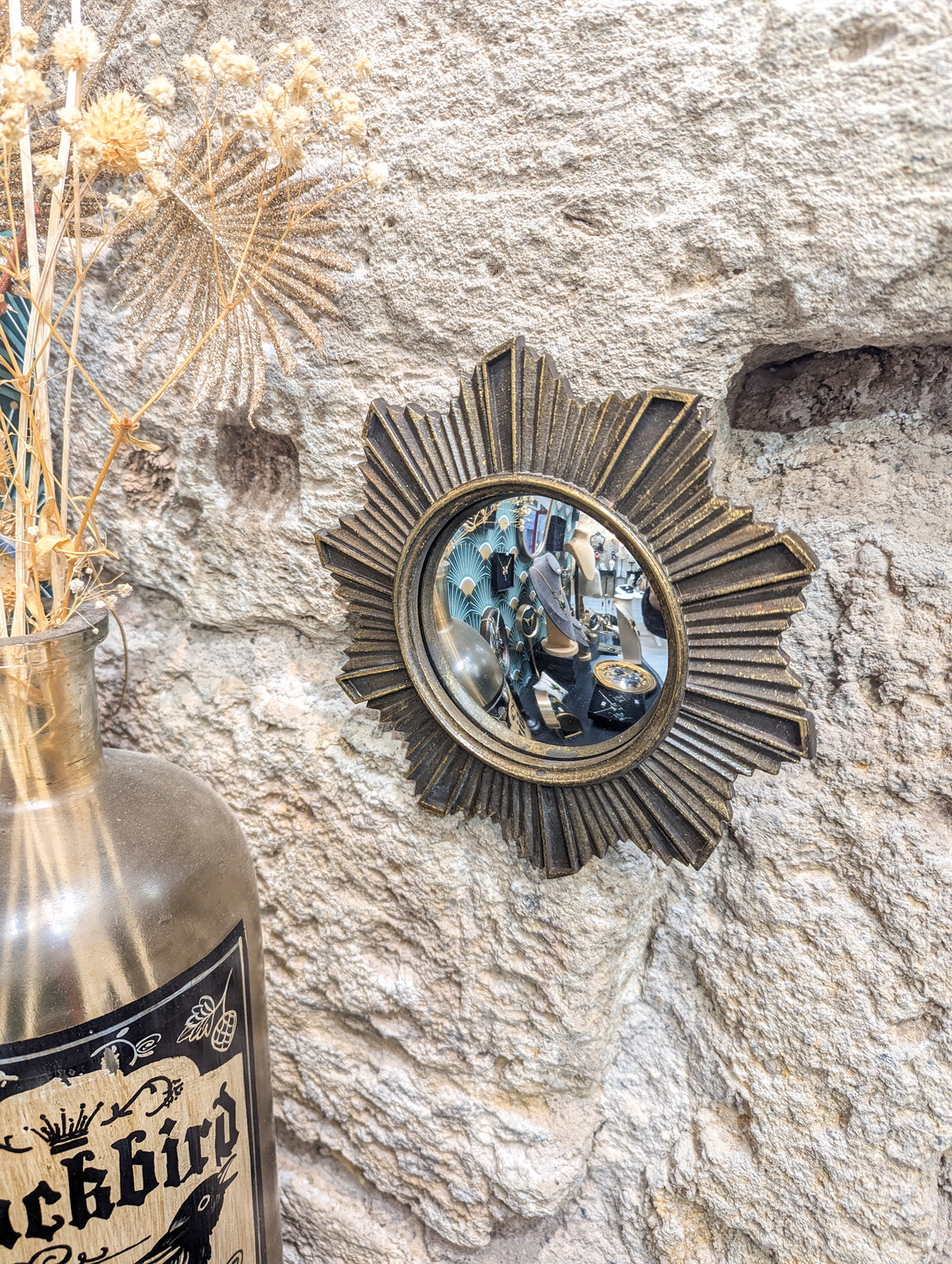 Miroir convexe soleil accroché sur un mur en pierre avec fleurs séchées