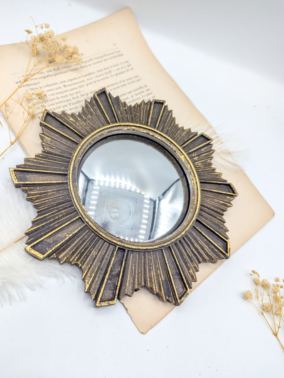 Miroir de sorcière soleil rayonnant posé sur un livre ancien