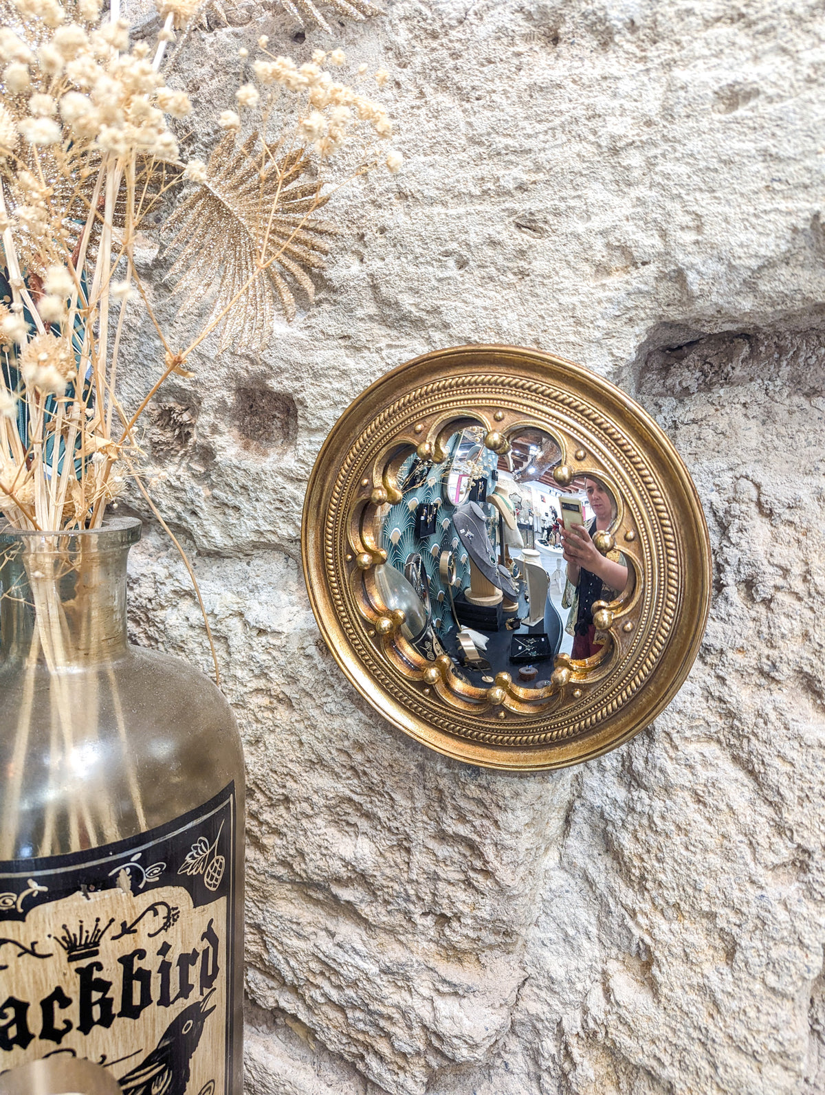 Miroir convexe doré à motifs de couronne, vue de biais sur mur en pierre