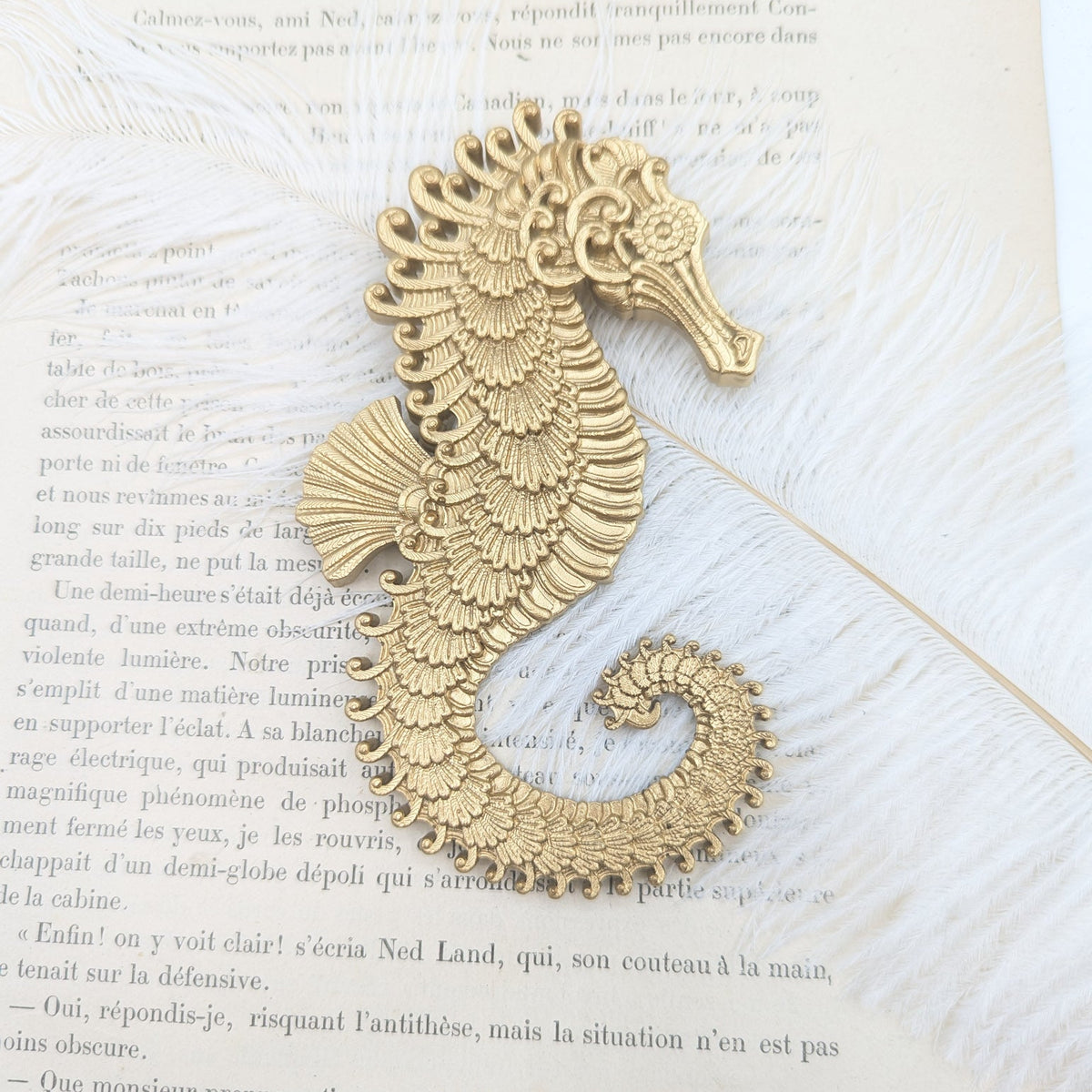 Hippocampe baroque doré posé sur un livre ancien avec plume