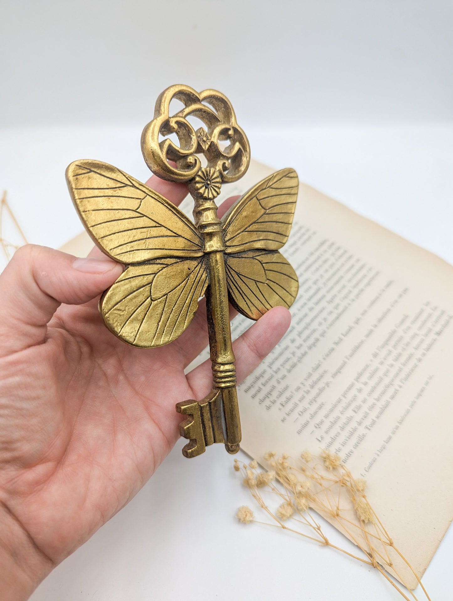 Une clé décorative en métal doré avec des ailes de papillon. Les ailes sont déployées, donnant un aspect fantaisiste. Idéal pour la décoration.