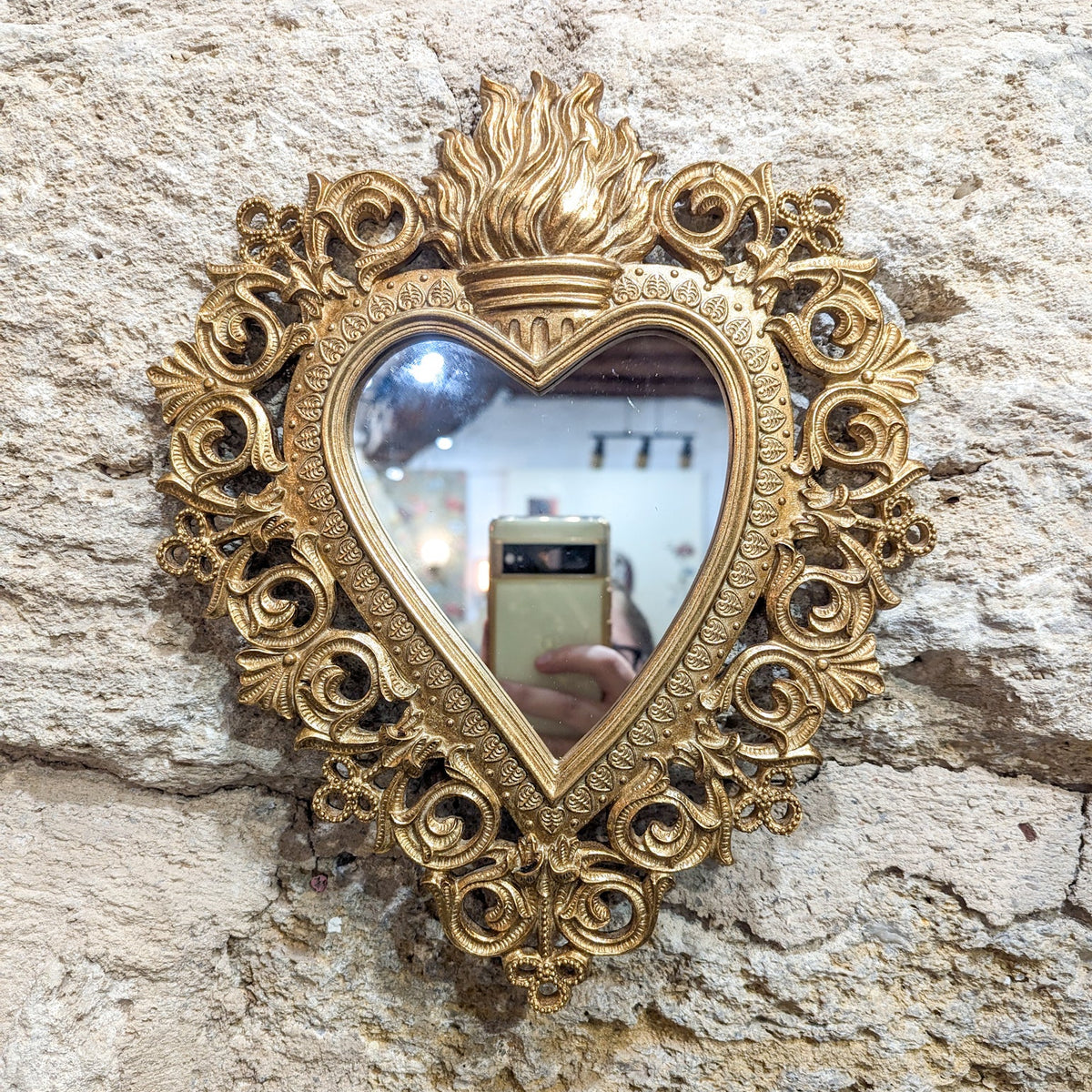Miroir cœur sacré ex-voto doré accroché sur un mur en pierre