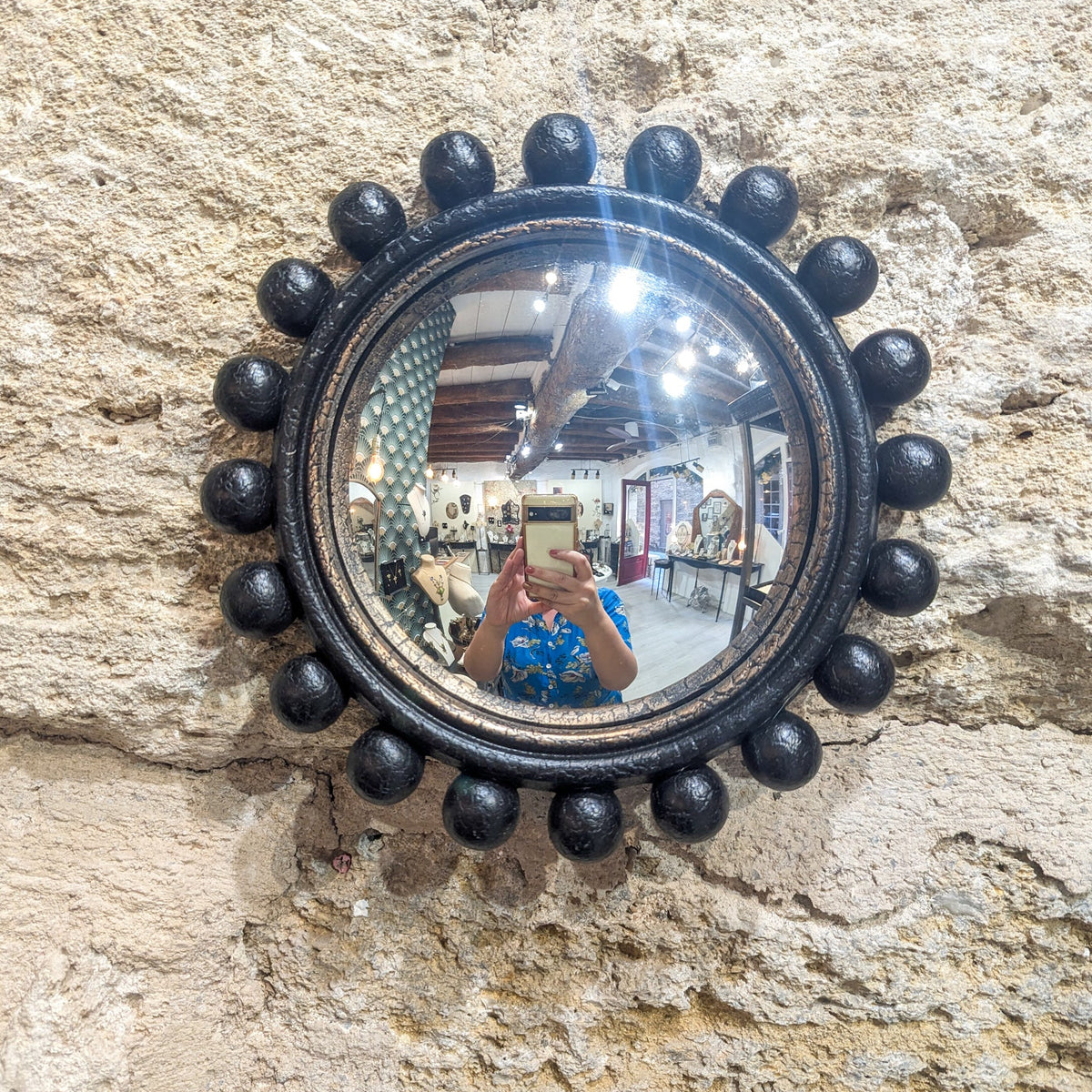 Miroir de sorcière noir à boules style Renaissance accroché sur un mur en pierre